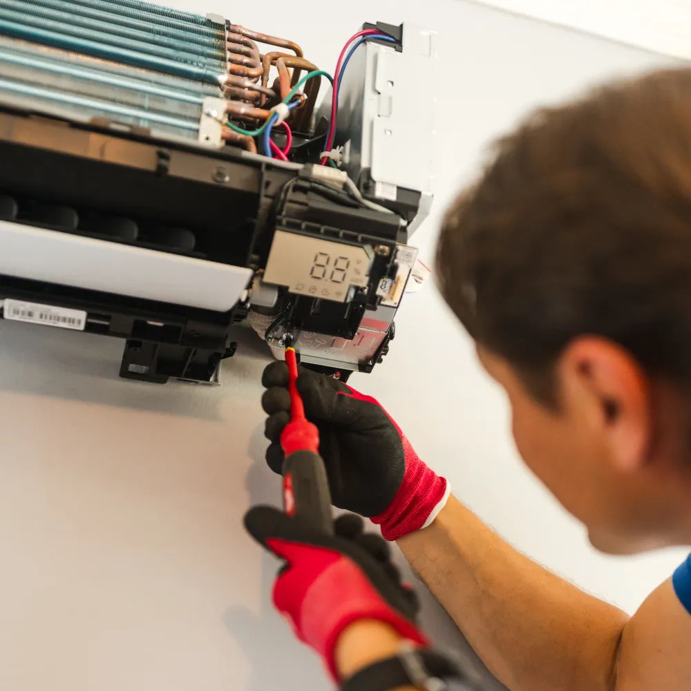 Technician in red gloves repairing an air conditioning unit mounted on a white wall.