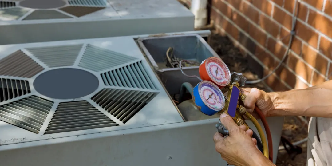 Person checks air conditioning unit outdoors with HVAC gauge manifold and hoses.