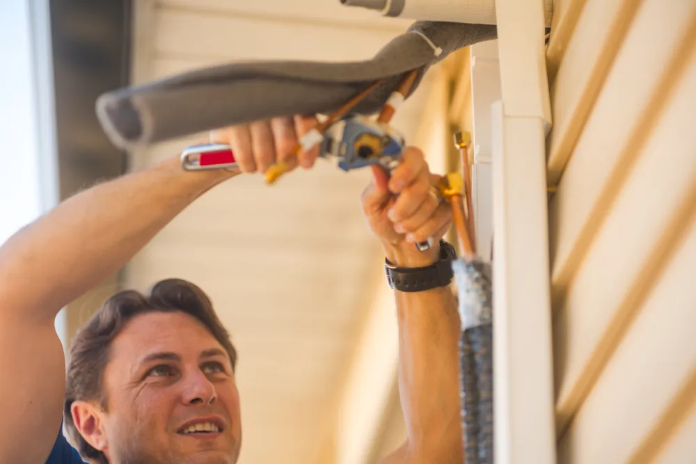 Man uses tool to install or repair an outdoor air conditioning unit on a house wall.