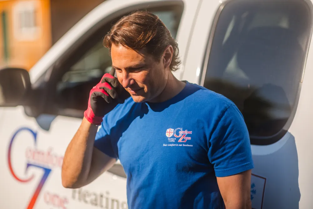 Man in blue shirt and red glove talking on phone in front of a white service van.
