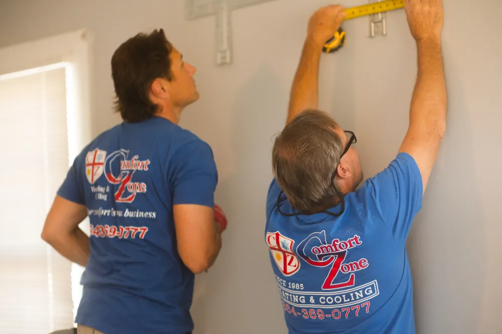 Two men in blue shirts measure a wall with a tape measure and pencil, preparing to install something.