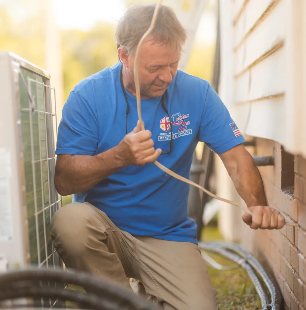 Man in blue shirt installing cables outside next to an air conditioning unit and a house wall.